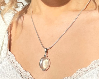 May include: A silver necklace with a pendant featuring an oval, iridescent stone. The pendant is suspended from a delicate chain. The necklace is worn against a white lace top.