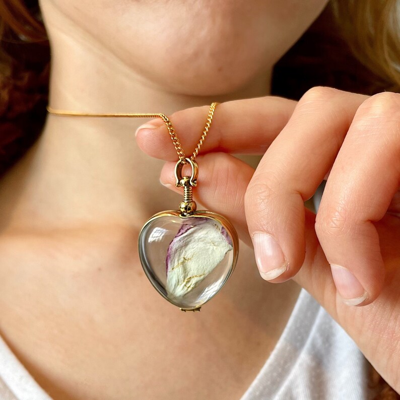 May include: A gold heart-shaped locket necklace with a clear glass pendant containing a dried rose petal.