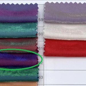 May include: Swatch card with a variety of fabric samples in different colors and textures. The card is numbered with rows and columns. The fabric samples are arranged in a grid pattern. The fabric sample in the third row and first column is a deep purple color with a slight sheen.
