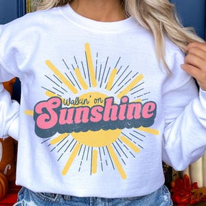 May include: White sweatshirt with a retro sun graphic and the text "Walkin' on Sunshine".