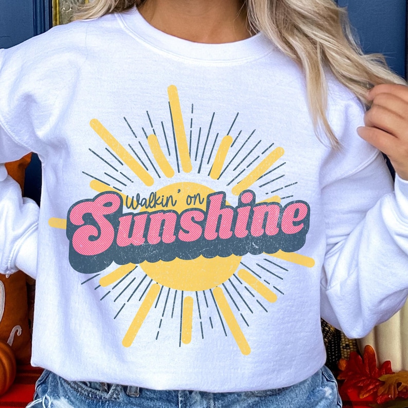 May include: White sweatshirt with a retro sun graphic and the text "Walkin' on Sunshine".