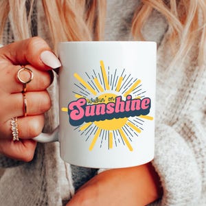 May include: White ceramic mug with a yellow sun and the text "Walkin' on Sunshine" in pink and blue letters.