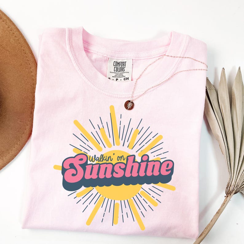 May include: Pink t-shirt with a retro-style graphic of a sun with the text "Walkin' on Sunshine".