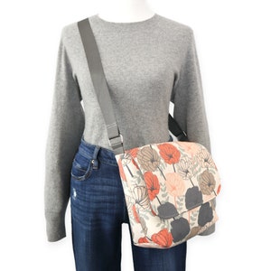 May include: A gray canvas messenger bag with a floral print featuring orange, pink, and brown flowers. The bag has a gray adjustable strap.