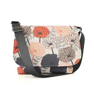 May include: A beige messenger bag with a black adjustable strap. The bag features a floral pattern with orange, pink, and gray flowers.