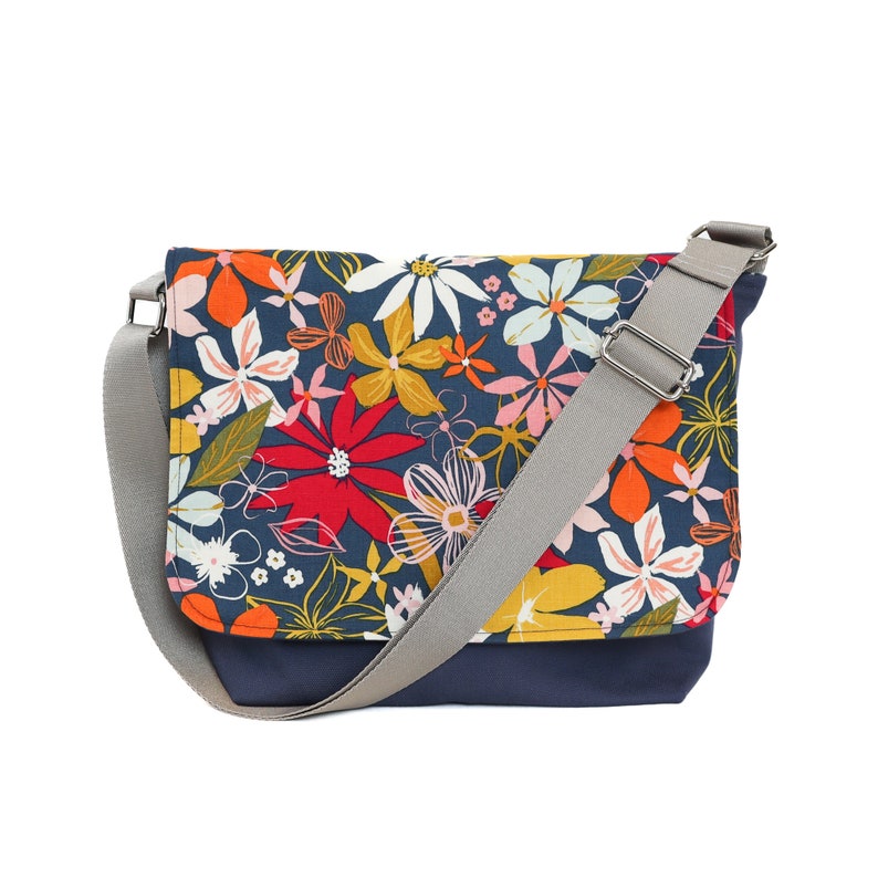 May include: A blue canvas messenger bag with a floral print featuring red, yellow, orange, and white flowers. The bag has a gray adjustable strap.