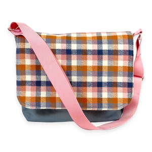 May include: A plaid messenger bag with a pink strap. The bag has a gray bottom and a plaid pattern in shades of orange, pink, blue, and white.