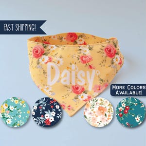 May include: Yellow floral dog bandana with the name "Daisy" in white. The bandana features a pattern of pink and red roses and white flowers. Additional color options are displayed below the bandana.
