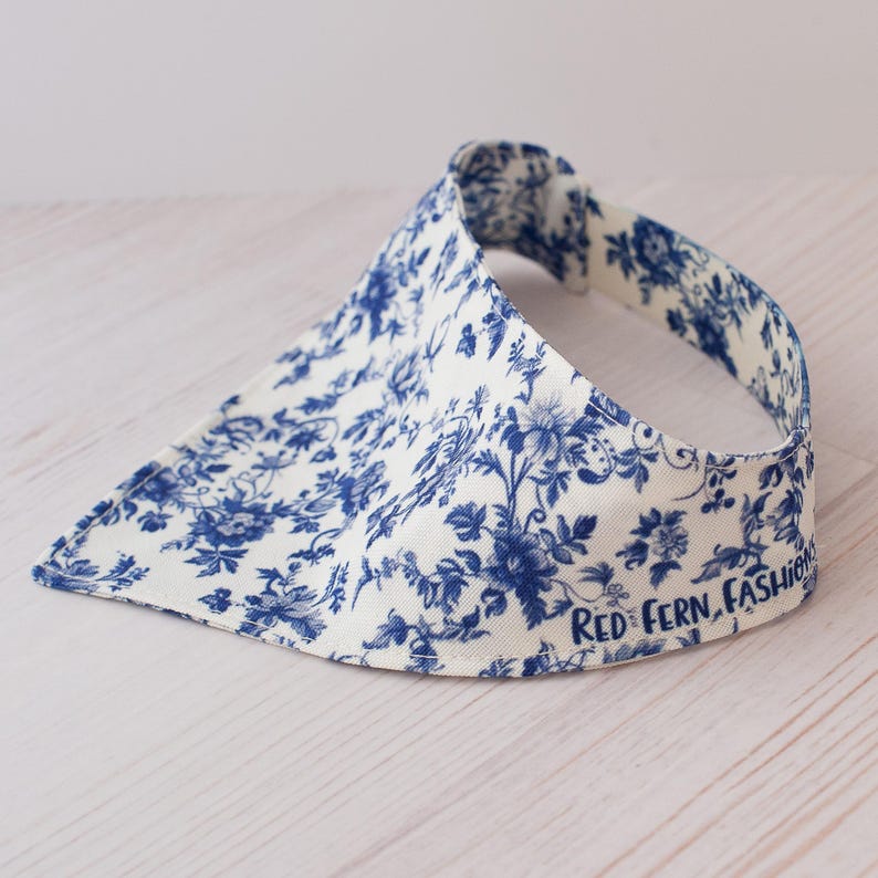 May include: A white visor with a blue floral pattern. The visor has a curved brim and a band that goes around the head. The text "RED FERN, FASHION" is printed on the side of the visor.
