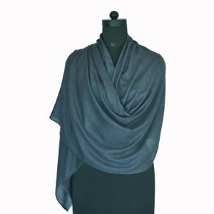 May include: A dark slate gray shawl draped over a mannequin. The fabric features a fine, lightweight texture with visible folds and soft drapes that wrap around the neck and shoulders, creating a layered appearance with a smooth finish.