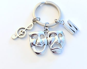 May include: Silver keychain with a treble clef charm, two theater masks, and a letter M charm.