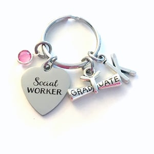 May include: Silver keyring with a heart charm that says "Social Worker", a graduation cap charm that says "Graduate", and a pink rhinestone charm.