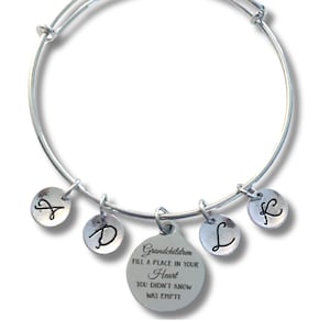 May include: A silver-toned expandable bangle bracelet featuring five circular charms. Four smaller charms are engraved with the letters A, D, L, and K. A larger central charm is engraved with the text: Grandchildren fill a place in your heart you didn't know was empty.