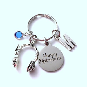 May include: Silver keychain with a blue gem, a charm that looks like headphones, a charm with the text "Happy Retirement", and a charm with the letter "M".