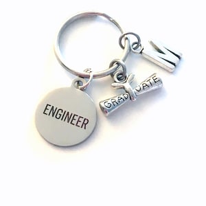 May include: Silver keychain with a round charm that says "Engineer", a graduation cap charm that says "Graduate", and a letter "M" charm.