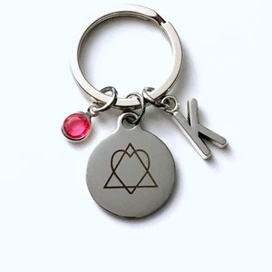 May include: Silver keychain with a round charm featuring a heart and star design, a red gemstone, and the letter "K". The keychain is on a white background.