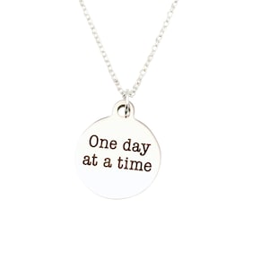 May include: Silver necklace with a round pendant that says "One day at a time".