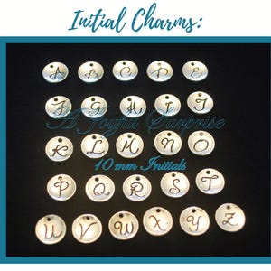 Könnte beinhalten: Eine Sammlung von sechsundzwanzig runden, silberfarbenen Metallanhängern, die jeweils mit einem einzelnen Buchstaben des Alphabets in Schreibschrift graviert sind. Der Text "Initial Charms:", "A Joyful Surprise" und "10 mm Initials" ist sichtbar.