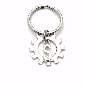May include: Silver keychain with a gear charm and the letter S in the center.