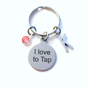 May include: A silver keyring with a round charm that says "I love to Tap". The keyring also has a small red rhinestone and a silver charm with the letter "K" on it.