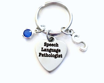 May include: A silver heart-shaped keychain with the text "Speech Language Pathologist" and a small blue gem charm. The keychain also has a silver letter "S" charm.
