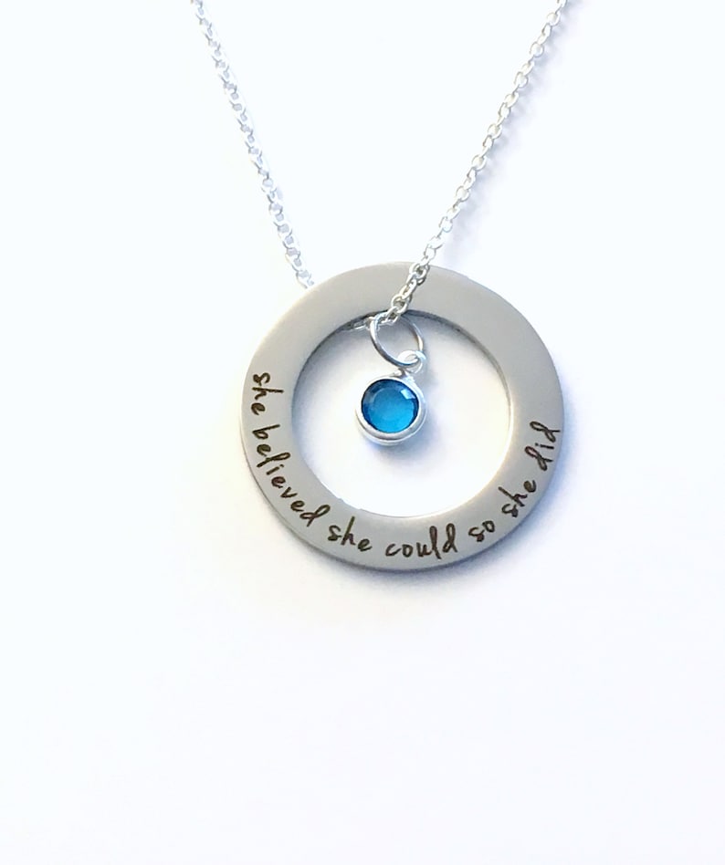 May include: Silver necklace with a round pendant that says "She believed she could so she did". A small blue gemstone hangs from the pendant.