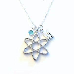 May include: Silver necklace with a silver atom charm, a blue gemstone, and a silver letter M charm.
