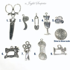 May include: Nine silver-toned metal charms with sewing-themed designs. The charms include scissors, a tape measure, a safety pin, a dress form, buttons, a sewing machine, yarn, and a dime for scale.