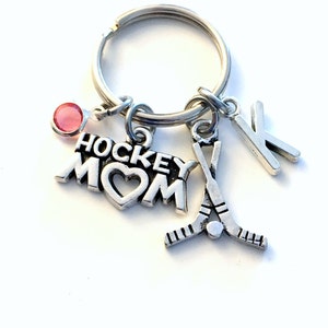 May include: Silver keychain with a hockey stick charm, a heart charm with the word "MOM" and the word "HOCKEY" above it, a pink rhinestone charm, and a letter "K" charm.