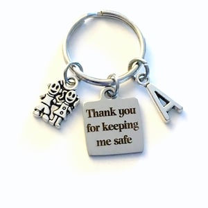 May include: Silver keychain with a square charm that says "Thank you for keeping me safe". There are also two small charms, one with a boy and girl holding hands and the other with the letter A.