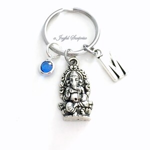 May include: Silver keychain with a blue crystal charm, a silver letter M charm, and a silver charm of the Hindu deity Ganesha.