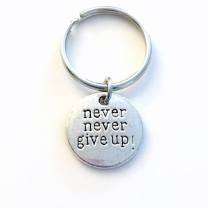Könnte beinhalten: Silberner Schlüsselanhänger mit einem runden Anhänger, auf dem "never never give up!" steht.