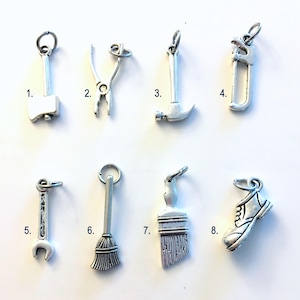 May include: A collection of eight silver-toned metal charms arranged in two rows, numbered one through eight. The charms depict an axe, pliers, a hammer, a hacksaw, a wrench, a broom, a paintbrush, and a shoe, each with a small jump ring attached.