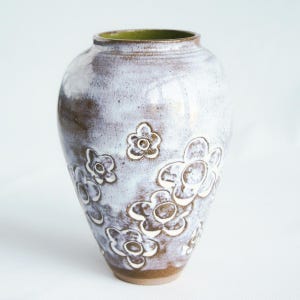 Peut inclure: Un vase en céramique avec un glaçage blanc et marron et des motifs de fleurs en relief. Le vase a un intérieur vert et une forme arrondie, adapté aux compositions florales ou comme pièce décorative.