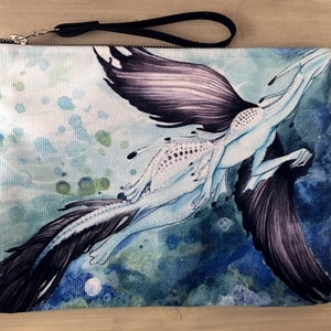 May include: A white canvas zippered pouch with a black strap. The pouch features a watercolor illustration of a blue and white creature with black wings, swimming in a blue and green ocean.