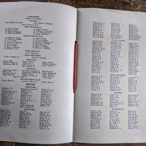 May include: Open book with a red string binding, featuring printed text in black ink. The pages display lists of names under headings like "Commanding," "Captains," and "First Lieutenants." The paper has a slightly aged, off-white color.