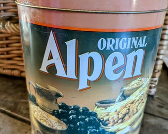 May include: A vintage metal tin container with a brown lid and a green, orange, and white label. The label says "Original Alpen" and features a depiction of grapes, wheat, and other ingredients.