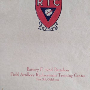 May include: A vintage document featuring a red and white shield emblem with the letters "RTC" and the word "LOCATE." Below the emblem, text reads "Battery F, 32nd Battalion, Field Artillery Replacement Training Center, Fort Sill, Oklahoma."