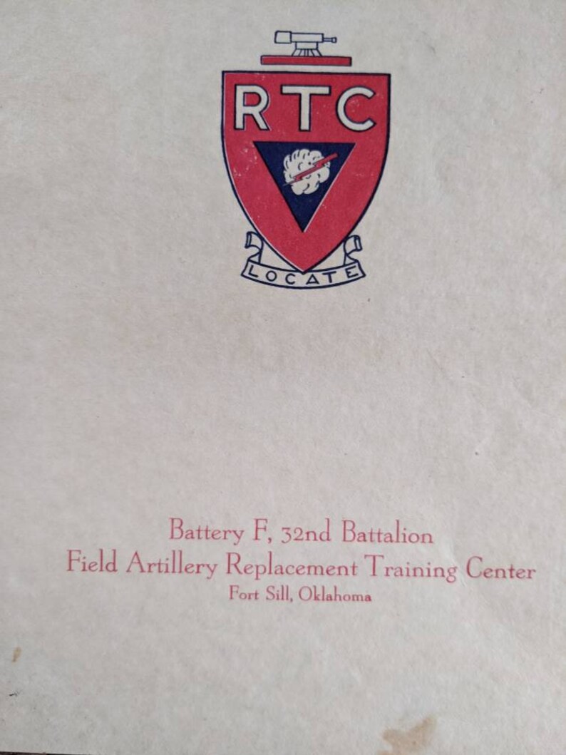 May include: A vintage document featuring a red and white shield emblem with the letters "RTC" and the word "LOCATE." Below the emblem, text reads "Battery F, 32nd Battalion, Field Artillery Replacement Training Center, Fort Sill, Oklahoma."