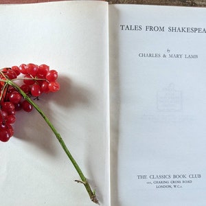 May include: An open book titled "Tales from Shakespeare" by Charles & Mary Lamb. The book is part of The Classics Book Club and is published in London, England. A sprig of red berries is on the left page.