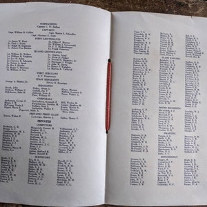 May include: An open book with a red string binding, featuring printed text organized into columns. The left page lists names under headings like "Commanding" and "First Lieutenants." The right page continues with more names and categories.