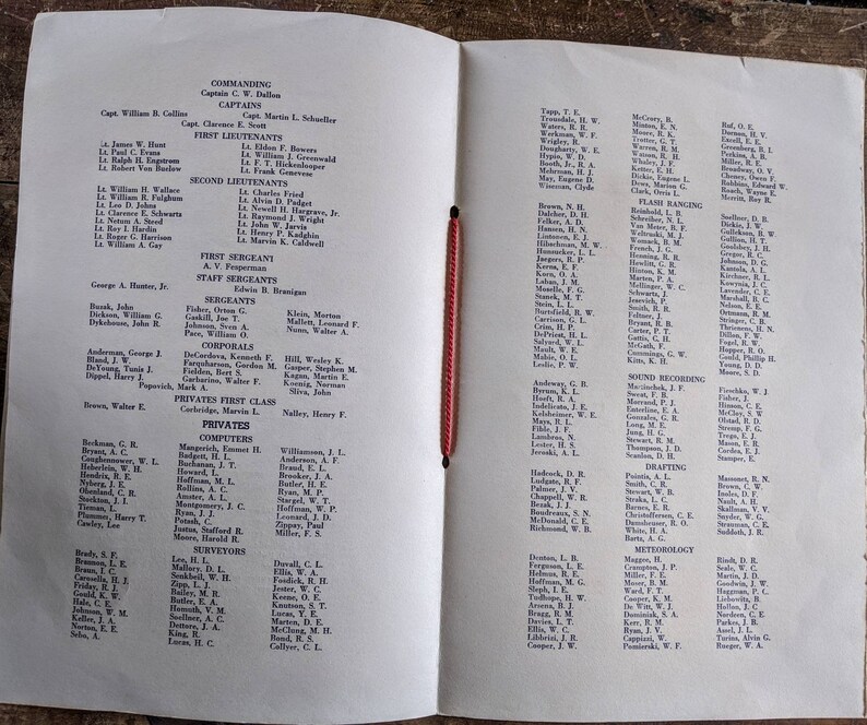 May include: An open book with a red string binding, featuring printed text organized into columns. The left page lists names under headings like "Commanding" and "First Lieutenants." The right page continues with more names and categories.