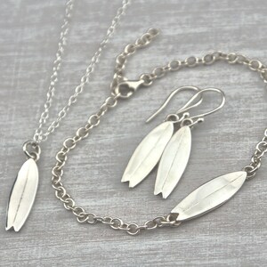 Op de afbeelding: Een set zilveren sieraden met surfplank bedels. De set bevat een ketting, armband en oorbellen.