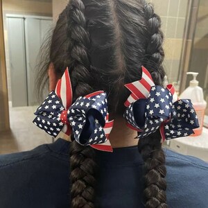May include: Two braided hairstyles with red, white, and blue star-patterned hair bows.