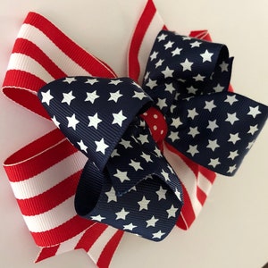 May include: A red, white, and blue bow with a star pattern. The bow is made of two different fabrics, one with stripes and one with stars.