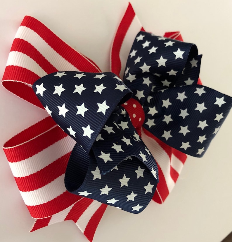 May include: A red, white, and blue bow with a star pattern. The bow is made of two different fabrics, one with stripes and one with stars.