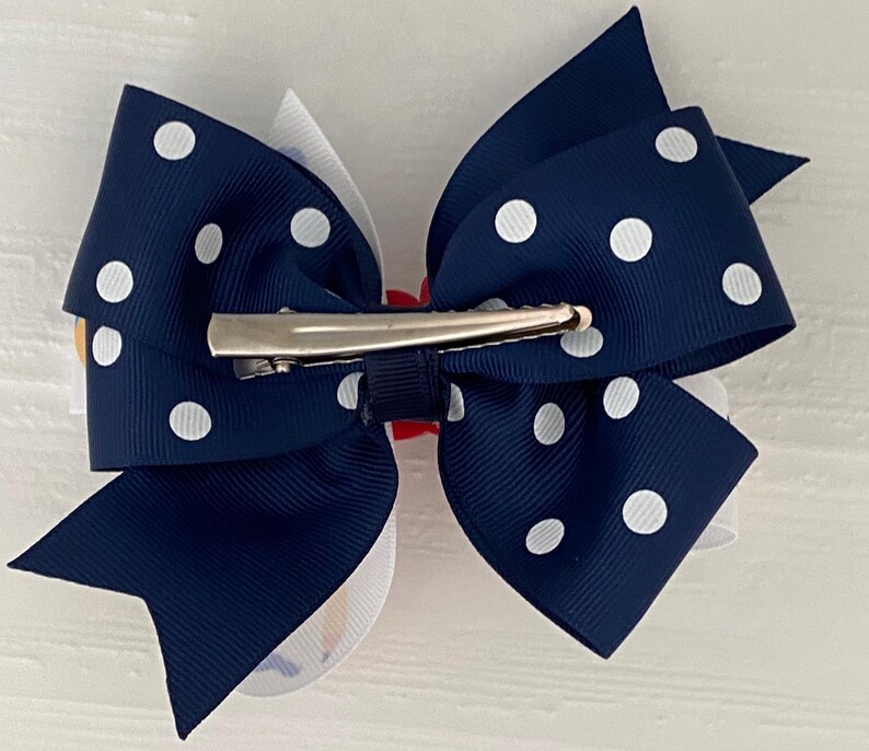 Op de afbeelding: Een navyblauwe haarstrik met witte stippen en een zilveren alligatorclip. De strik is in een klassieke stijl geknoopt met een wit midden.