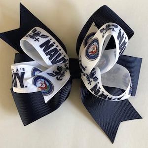May include: A navy blue and white hair bow with the words "America's Navy" and a navy seal emblem.