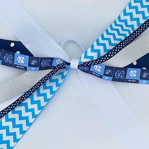 May include: A blue and white hair bow with a chevron pattern, white polka dots, silver glitter ribbon, and a blue and white ribbon with the text "Tar Heels".