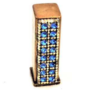 May include: A gold-colored rectangular box with a decorative design of blue gemstones. The box is small and appears to be a decorative item.